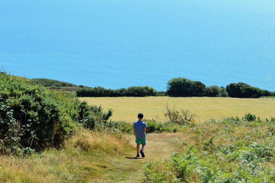Harrison walking down a grassy path towards the sea.