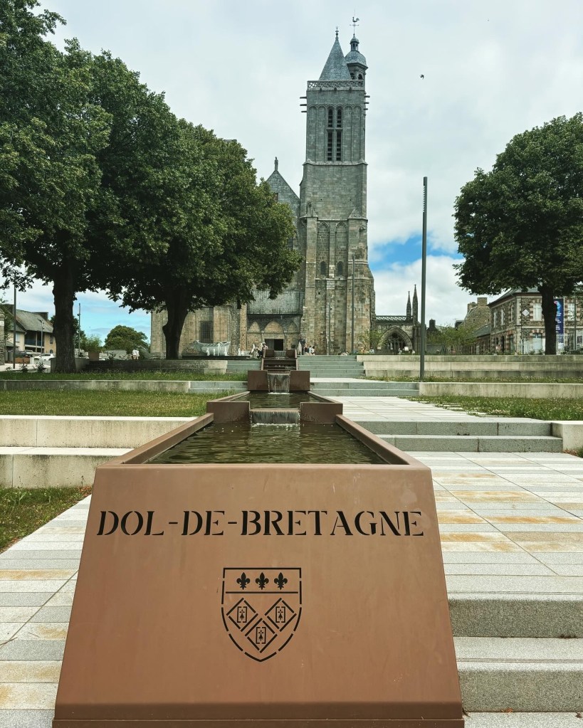 Bronze inscription Dol-de-Bretagne on the end of a water feature which cascades down steps from a cathedral.