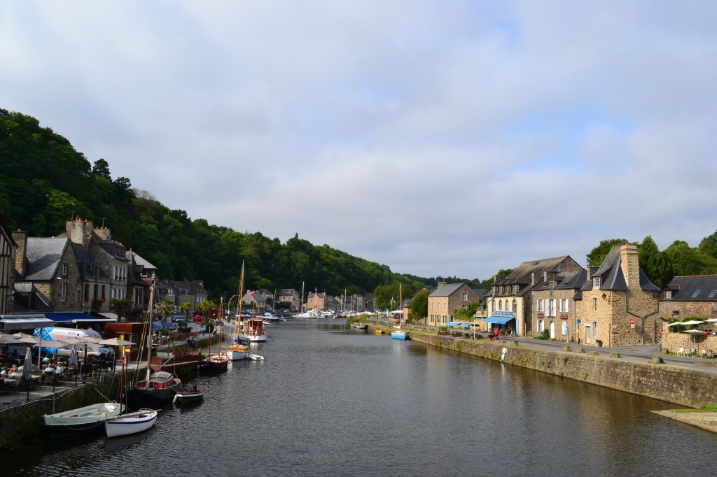 A river with sailing boats and tree covered hills behind it.