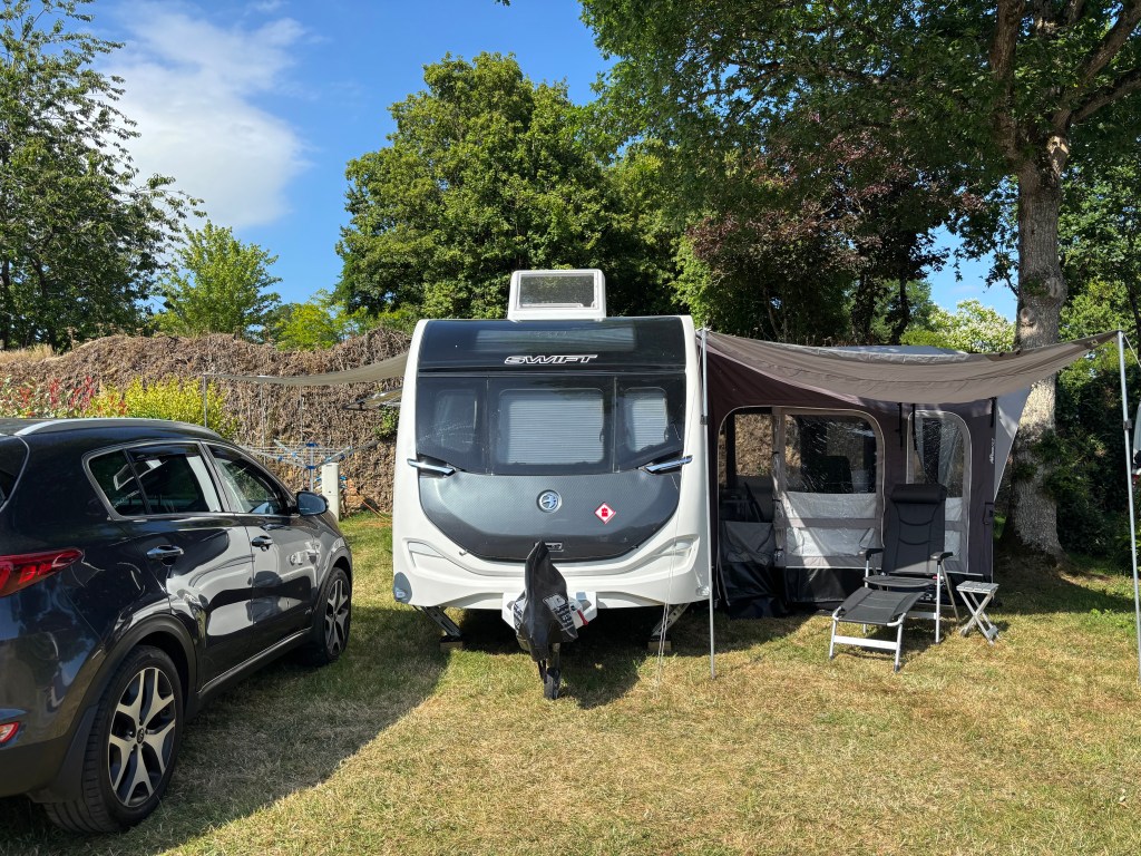 Car parked next to a caravan which has an awning and sun canopies, with a chair outside.