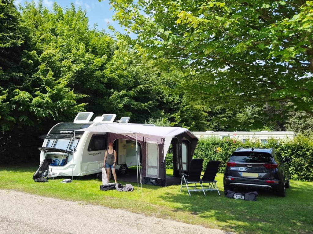 Claire standing in front the awning of the caravan, surrounded by trees and on grass.